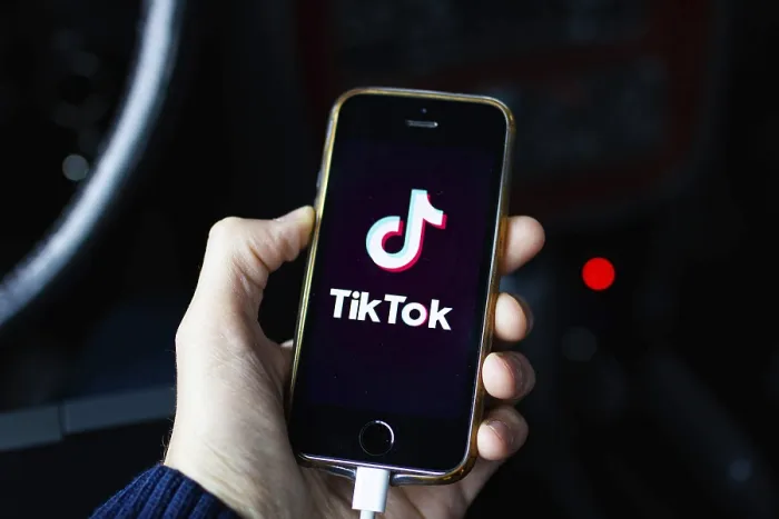 Framed Print : A hand holding a smartphone displaying the TikTok app on a dark background