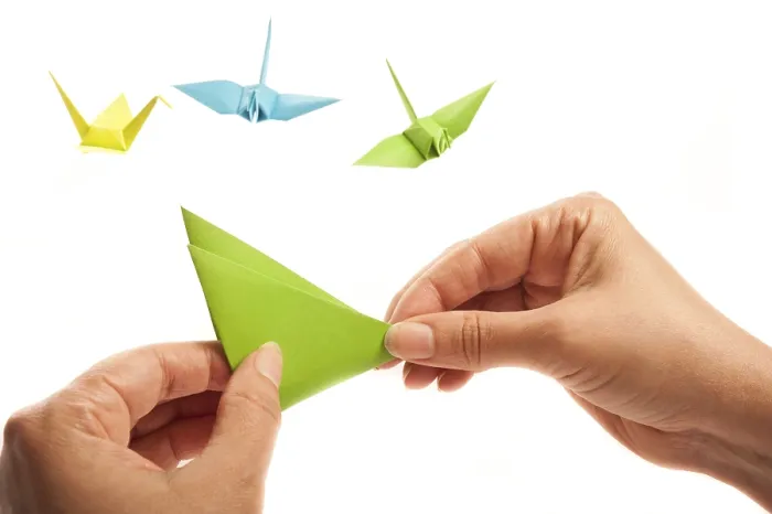 Framed Print : Hands crafting an origami piece with colorful cranes in the background