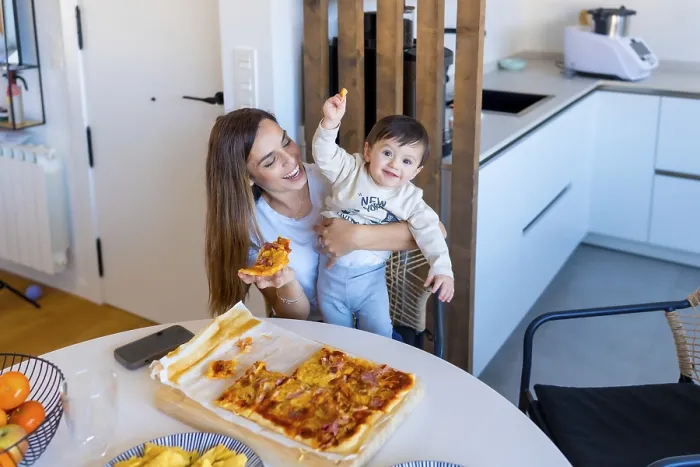 Framed Print : Happy mother holding her baby while eating pizza in a bright