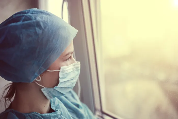 Framed Print : A healthcare worker in scrubs and a mask gazes out the window at sunset