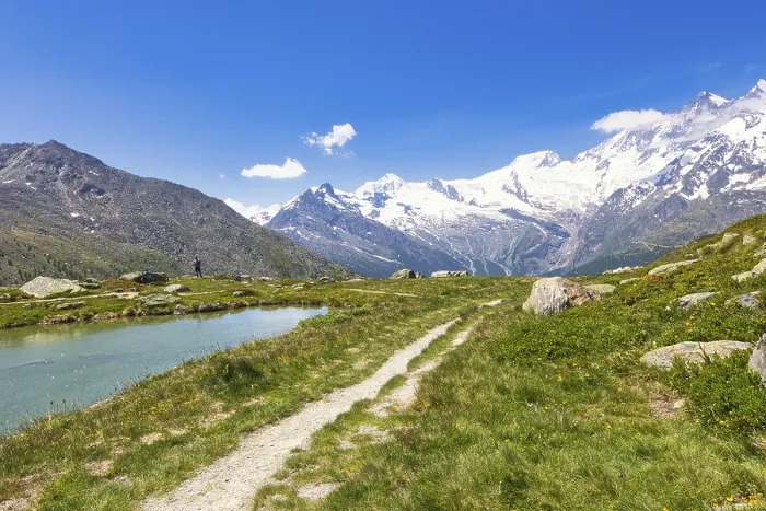 Framed Print : Hiking trail leads along a clear stream to snow-crowned mountains