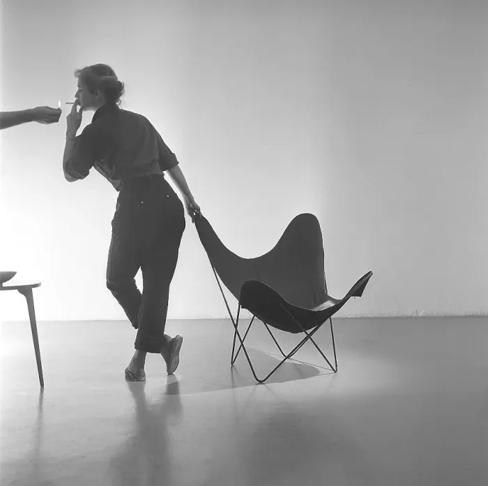 Framed Print : Home decor of the 1950s. A young woman is standing beside the popular Butterfly chair Framed Print : Home decor of the 1950s. A young woman is standing beside the popular Butterfly chair