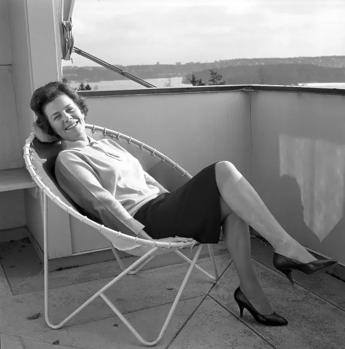 Framed Print : Home decor of the 1960s. A woman is sitting comfortably in the 1950s 1960s deck chair designed with steel pipes with a round center and four legs. The seat is made of leather Framed Print : Home decor of the 1960s. A woman is sitting comfortably in the 1950s 1960s deck chair designed with steel pipes with a round center and four legs. The seat is made of leather