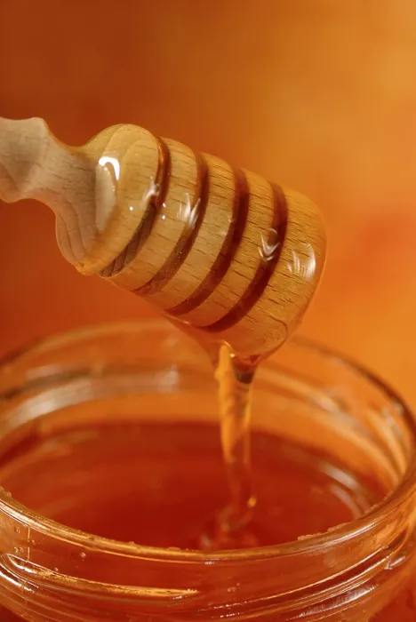 Framed Print : A honey dipper with viscous honey is placed over a jar against a golden amber background Framed Print : A honey dipper with viscous honey is placed over a jar against a golden amber background