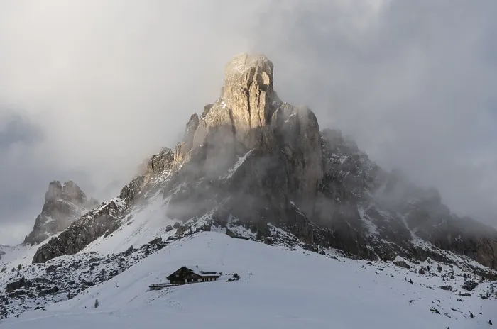 Framed Print : A hut is located under huge, snow-covered mountain peaks and clouds on Passo di Giau