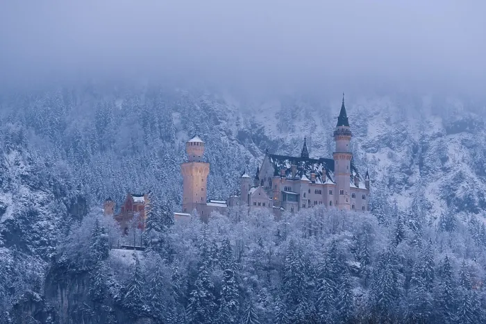 Framed Print : An illuminated castle at dusk, surrounded by snow-covered trees and fog
