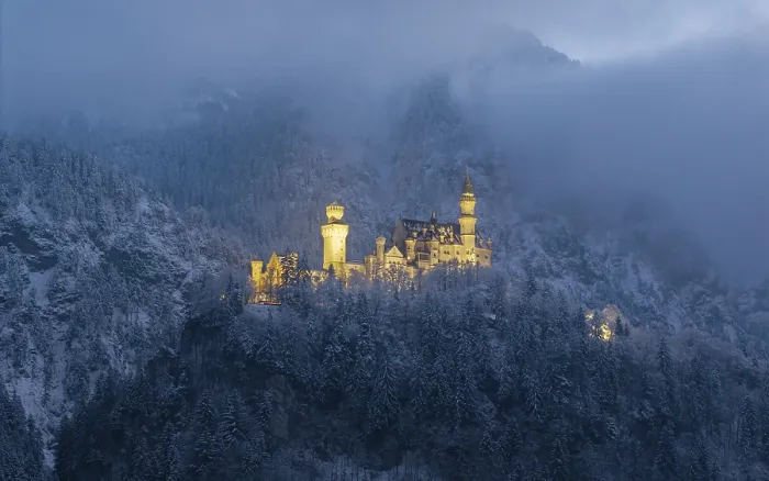 Framed Print : Illuminated castle surrounded by snow-covered mountains in a gloomy atmosphere