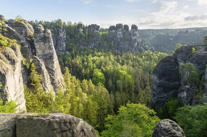Framed Print : Impressive rock formations and thick green forests in sunshine under a cloudy sky in Saxon Switzerland National Park
