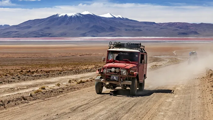 Framed Print : A jeep drives dusty on a desert road with mountains in the background