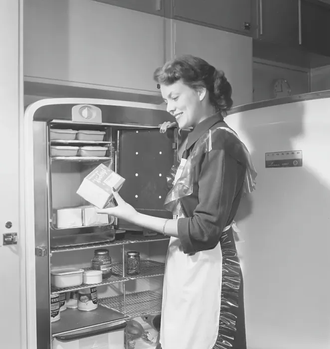 Framed Print : In the kitchen 1950s. Interior of a kitchen and a young woman standing at the Leonard refrigirator with it's door open, showing the cans and bottes of different food standing on the shelfes Framed Print : In the kitchen 1950s. Interior of a kitchen and a young woman standing at the Leonard refrigirator with it's door open, showing the cans and bottes of different food standing on the shelfes