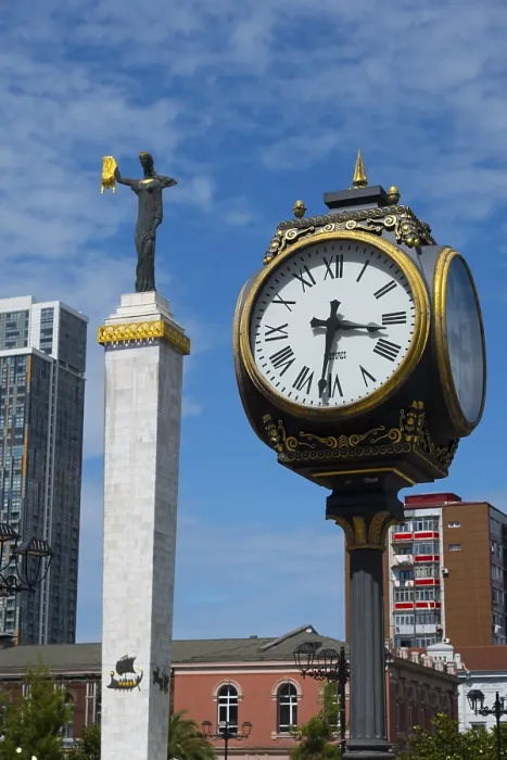 Framed Print : Large clock and statue in front of modern buildings under bright blue sky