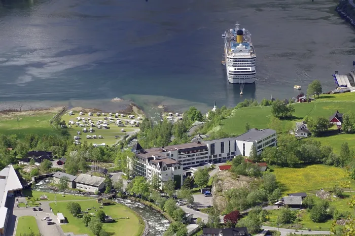 Framed Print : A large cruise ship is moored on a shore with many buildings and green meadows and trees