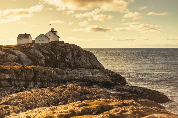 Framed Print : A lighthouse and house on rocky cliffs by the ocean at sunset Framed Print : A lighthouse and house on rocky cliffs by the ocean at sunset