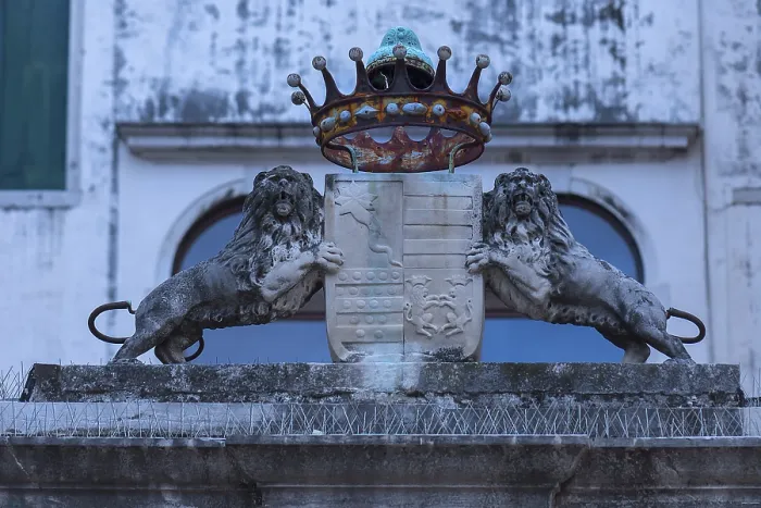 Framed Print : Two lion sculptures with a coat of arms and crown in front of a palazzo