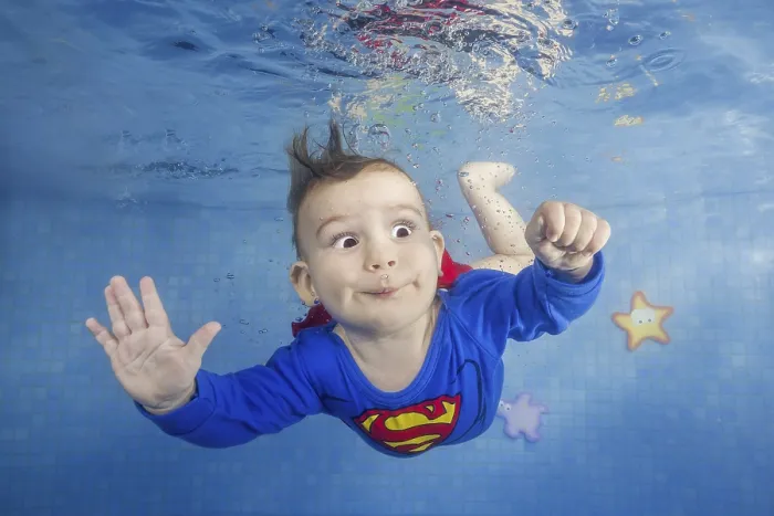 Framed Print : Little boy in a superman costume dives underwater in the pool