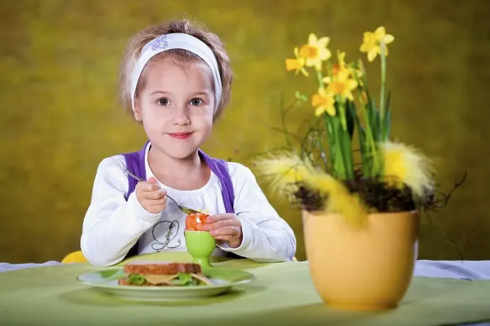 Framed Print : Little girl eating an Easter egg at a table