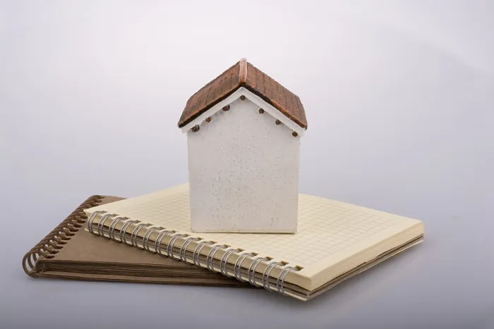 Framed Print : Little model house placed on an a brown color notebook