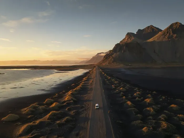 Framed Print : A lone car travels down a long dirt road flanked by dramatic mountainous terrain at sunset