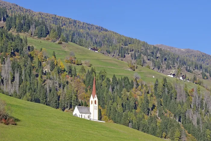 Framed Print : Lonely church with red tower on green alpine slope under bright blue sky