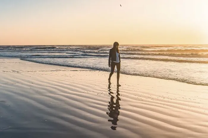 Framed Print : A lonely woman at the beach walking barefooted by the shore at sunrise