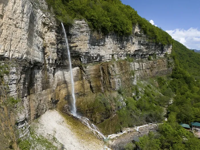 Framed Print : Long waterfall falls over a rock face into a wooded area under a clear sky