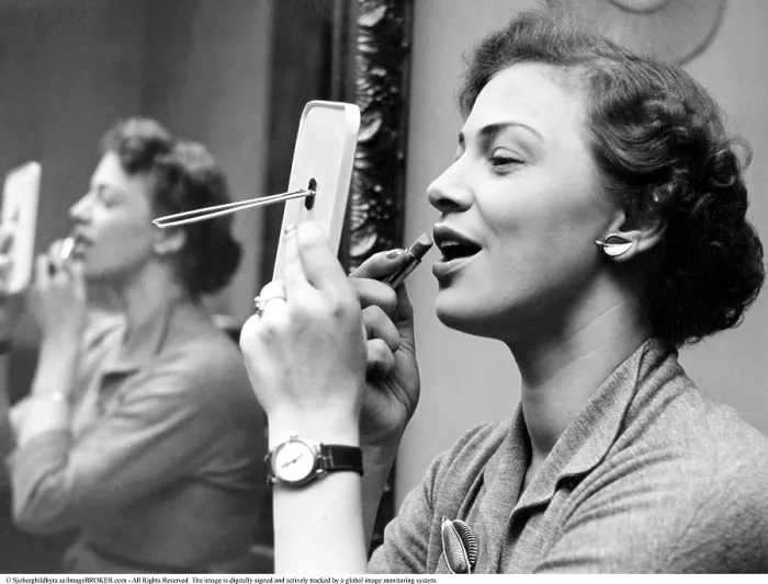 Framed Print : Looking good in the 1950s. She is looking at herself in the pocket mirror while applying lipstick