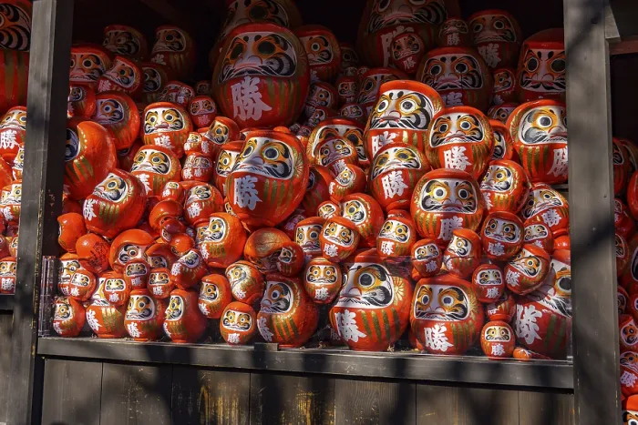 Framed Print : Lots of red Daruma dolls stacked in various sizes on a shelf in a Japanese temple