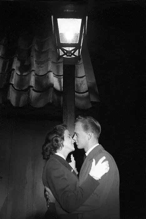 Framed Print : Love in the 1950s. A young couple in the evening are standing under a street lamp kissing Framed Print : Love in the 1950s. A young couple in the evening are standing under a street lamp kissing
