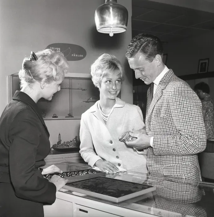 Framed Print : Love in the 1950s. A young couple at a jewelry shop is selecting wedding rings. A female sales clerk is standing at the counter with a case of many different models of rings. Kristoffersson ref CG35 Framed Print : Love in the 1950s. A young couple at a jewelry shop is selecting wedding rings. A female sales clerk is standing at the counter with a case of many different models of rings. Kristoffersson ref CG35