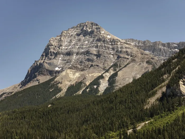 Framed Print : Majestic mountain peak with rocky slopes towering over a dense forest under a clear sky in British Columbia