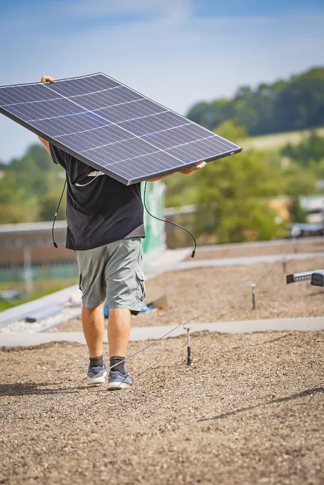 Framed Print : Man carrying solar panel on a gravel roof in front of a natural landscape