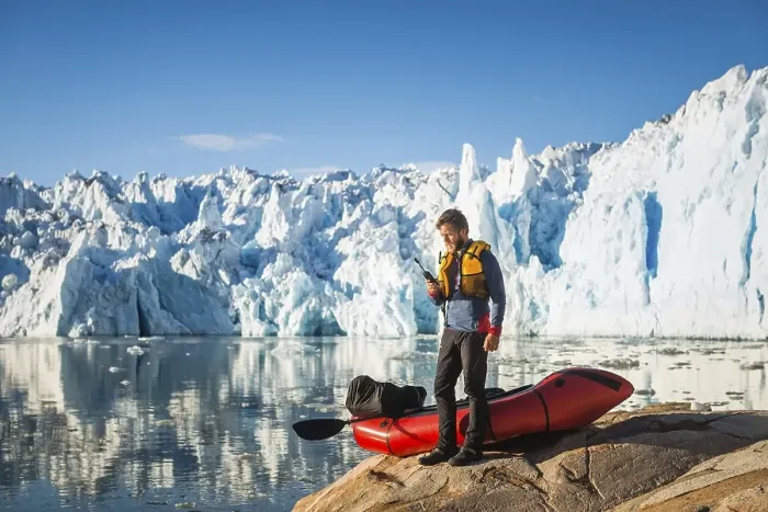 Framed Print : Man with packraft on fjord, satellite phone in hand