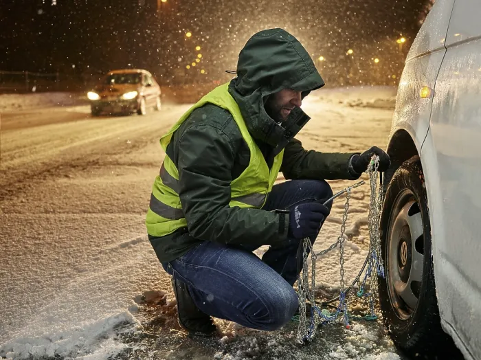 Framed Print : Man with safety vest applying snow chains on snow-covered road Framed Print : Man with safety vest applying snow chains on snow-covered road