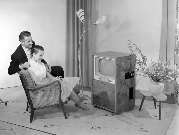 Framed Print : Man and woman sitting on an arm chair in front of a television