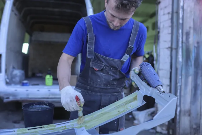 Framed Print : Man in workshop overalls paints a car part with a brush in a workshop Framed Print : Man in workshop overalls paints a car part with a brush in a workshop