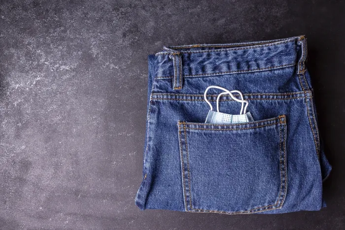 Framed Print : A medical mask peeks out from a jeans pocket on a black background