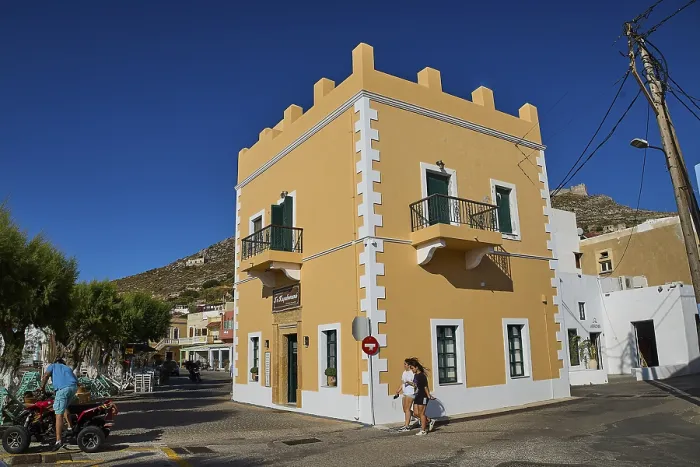 Framed Print : Mediterranean-style corner building with balconies and passers-by under a clear blue sky