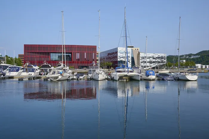 Framed Print : Modern buildings in red and white and boats in the harbour reflected in the calm water