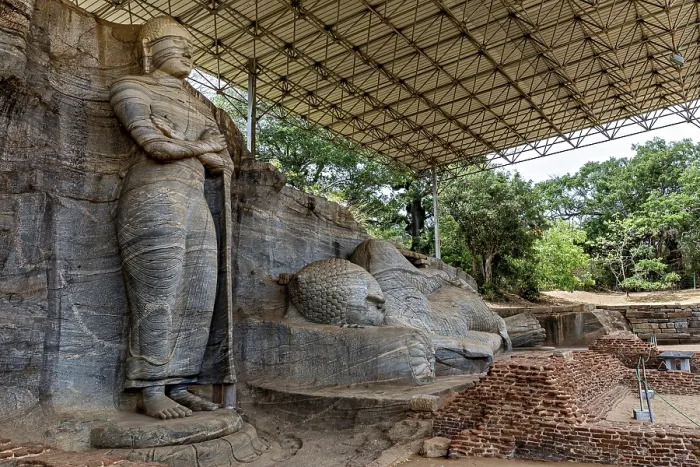 Framed Print : Monumental rock statue with standing and resting figure under a canopy surrounded by nature and brick walls