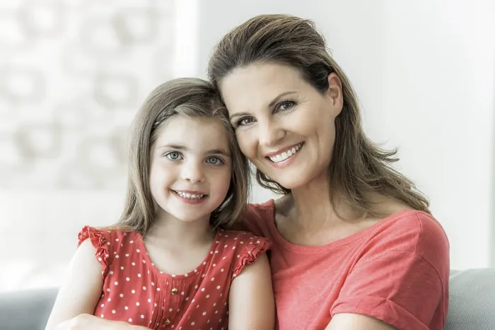 Framed Print : Mother and daughter sit together on the couch and look into the camera Framed Print : Mother and daughter sit together on the couch and look into the camera