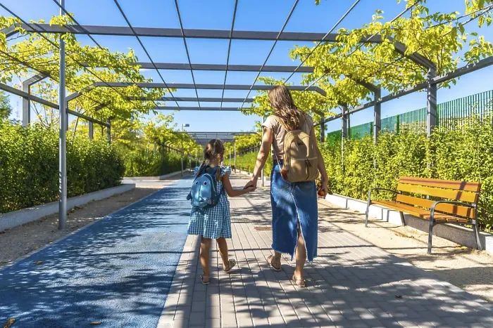 Framed Print : Mother and daughter walk hand in hand along an urban park path with backpacks Framed Print : Mother and daughter walk hand in hand along an urban park path with backpacks