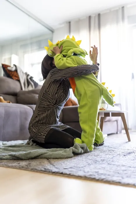Framed Print : Mother kneeling on carpet and hugging her son wearing a dinosaur costume while playing together in the living room