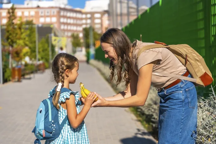 Framed Print : Mother smiles as she hands her schoolgirl a banana on a sunny walk