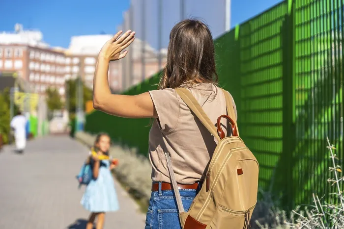 Framed Print : Mother waving goodbye, watching her young daughter with a backpack walk independently towards school