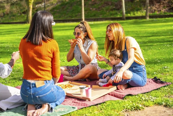 Framed Print : Mothers, friends and children are sharing a pizza during a picnic in a park