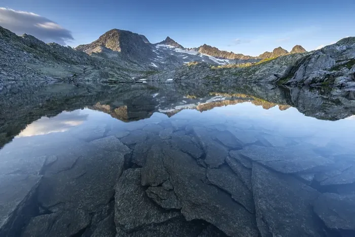 Framed Print : Mountain peaks and rocks reflected in the clear water of a lake at sunrise