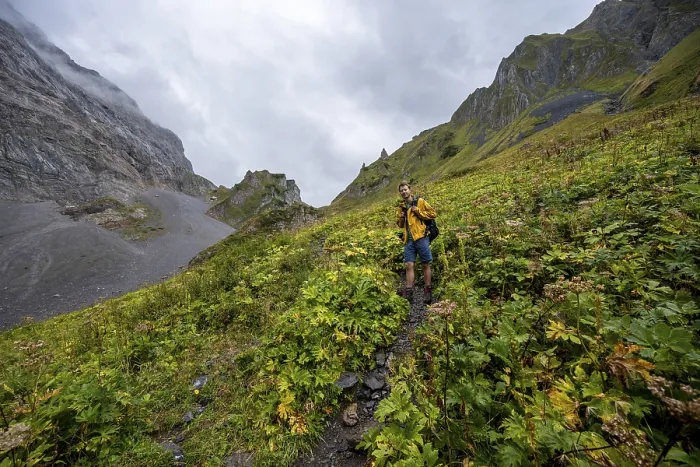 Framed Print : A mountaineer on a path surrounded by green vegetation and cloudy sky