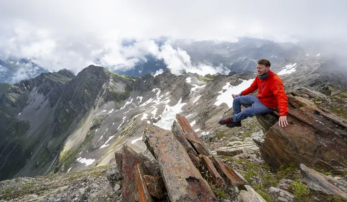 Framed Print : Mountaineer sitting on a rock, cloudy mountain landscape at the summit of Lasoerling