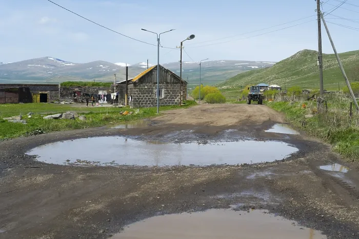 Framed Print : A muddy road with large puddles leads through a village with mountains in the background Framed Print : A muddy road with large puddles leads through a village with mountains in the background