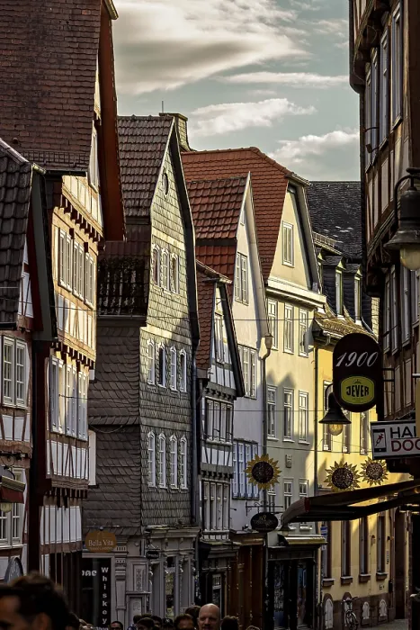 Framed Print : Narrowly built street with historic half-timbered houses and people passing by in the evening light